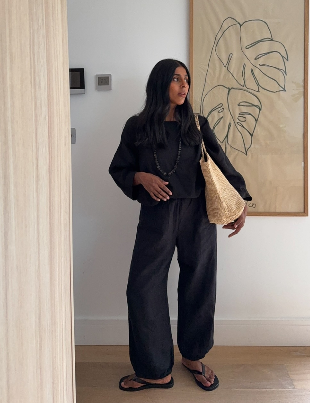 Moça em look preto descontraído, usando chinelo preto e carregando bolsa de palha. Inspiração de looks com chinelo preto.