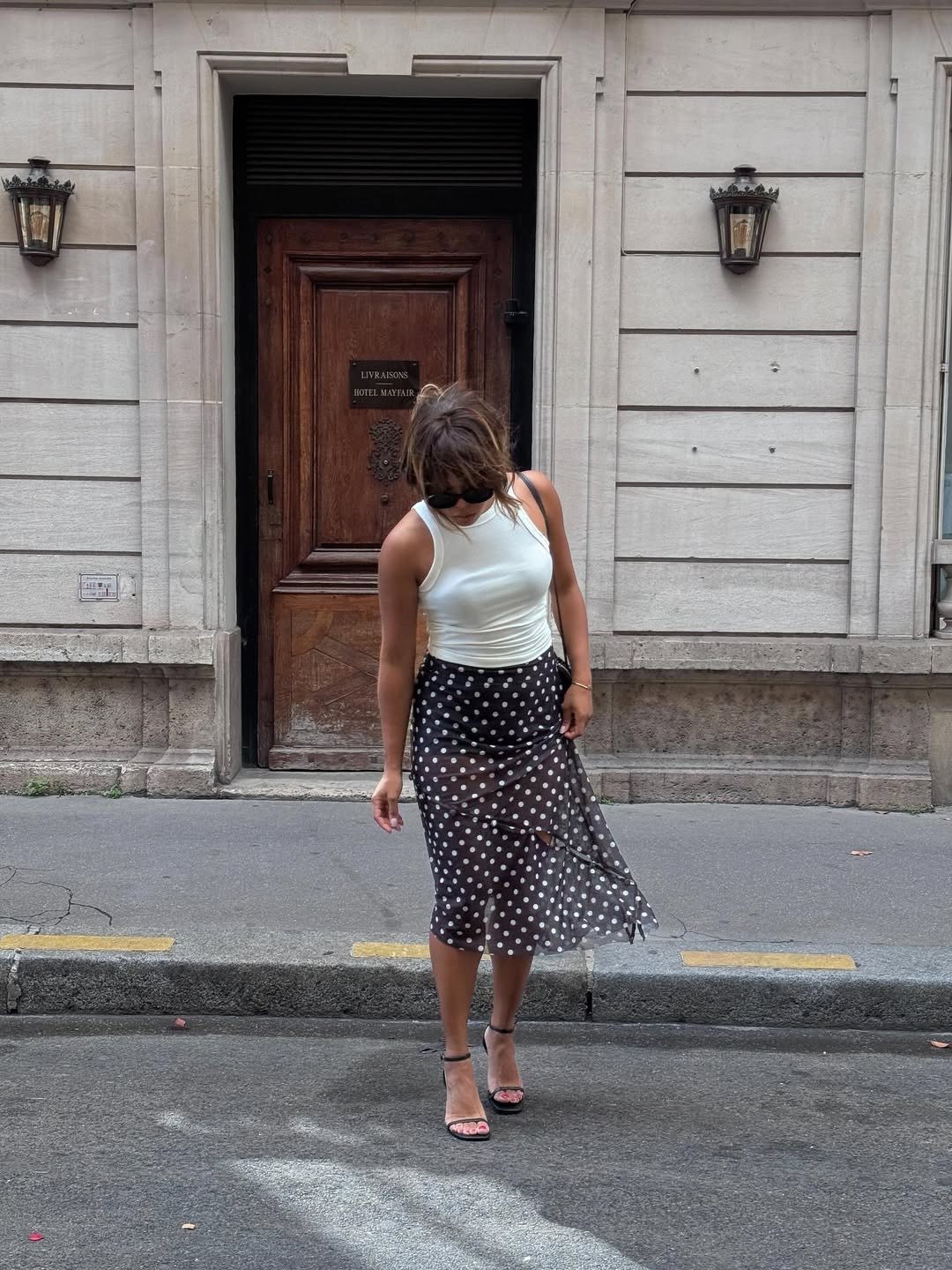 O look com regata é composto por uma regata branca, que traz um ar fresco e moderno, combinada com uma saia midi de tule com estampa de bolinhas pretas, ideal para ocasiões casuais ou eventos mais descontraídos. O uso de sandálias de tiras complementa o v