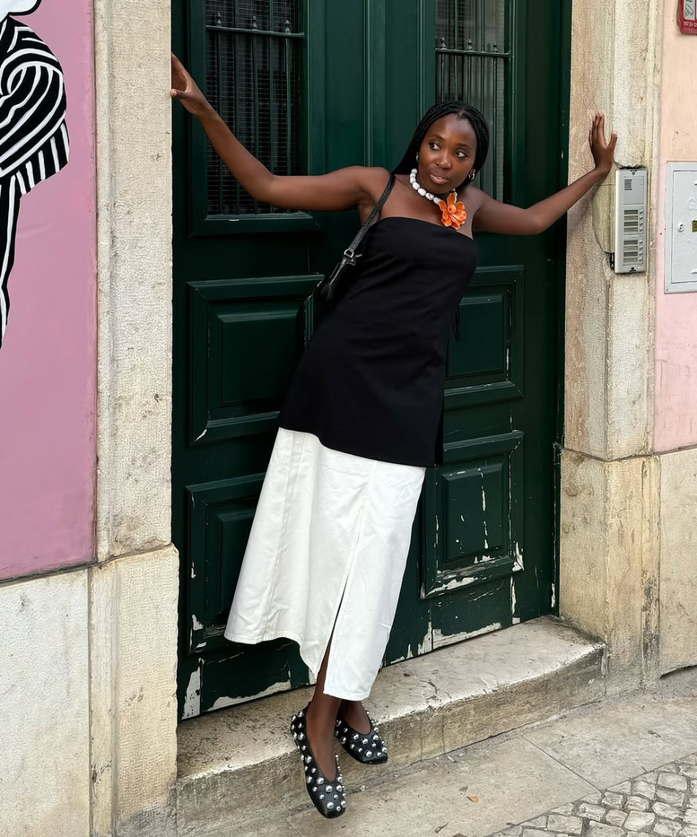 Mulher de vestido preto e branco posa em frente a uma porta verde, usando sapatilha com tachas.