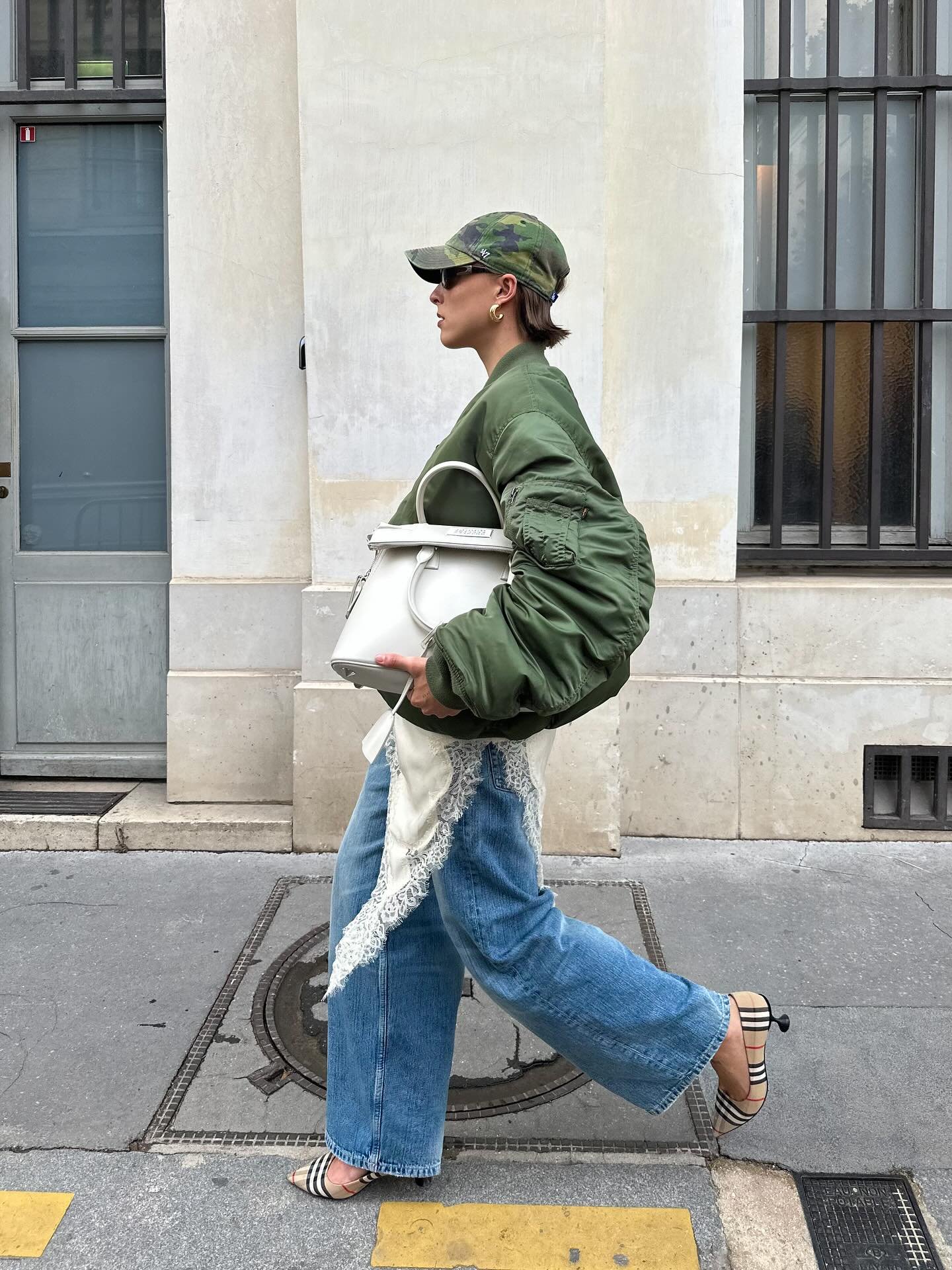 Pessoa usando calça jeans, slip dress assimétrico com renda e jaqueta verde, carregando bolsa branca grande.