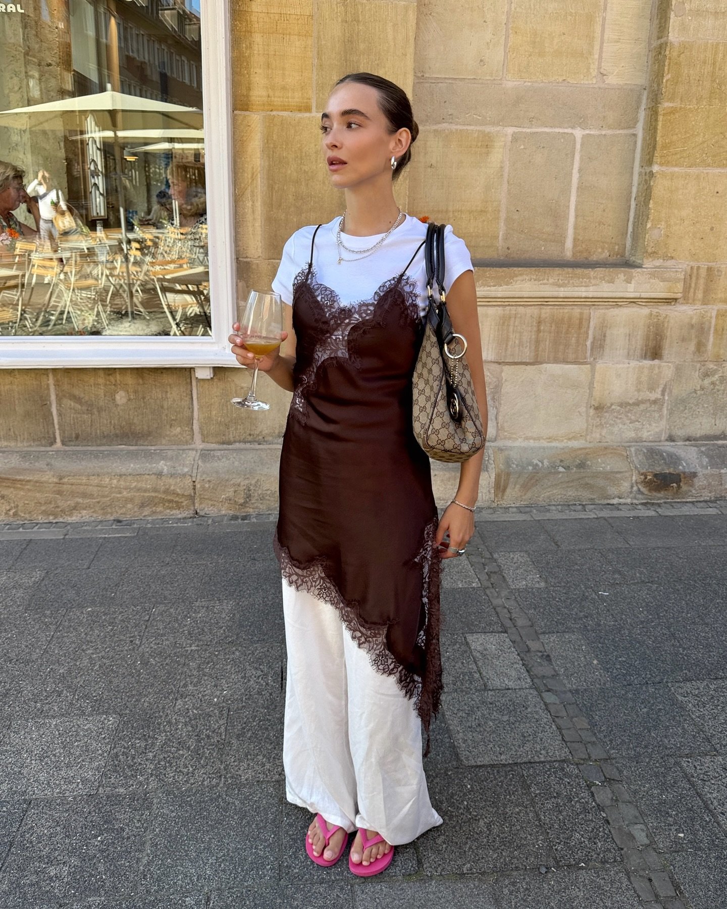 Pessoa usando slip dress assimétrico sobre camiseta branca, segurando taça de vinho e bolsa.