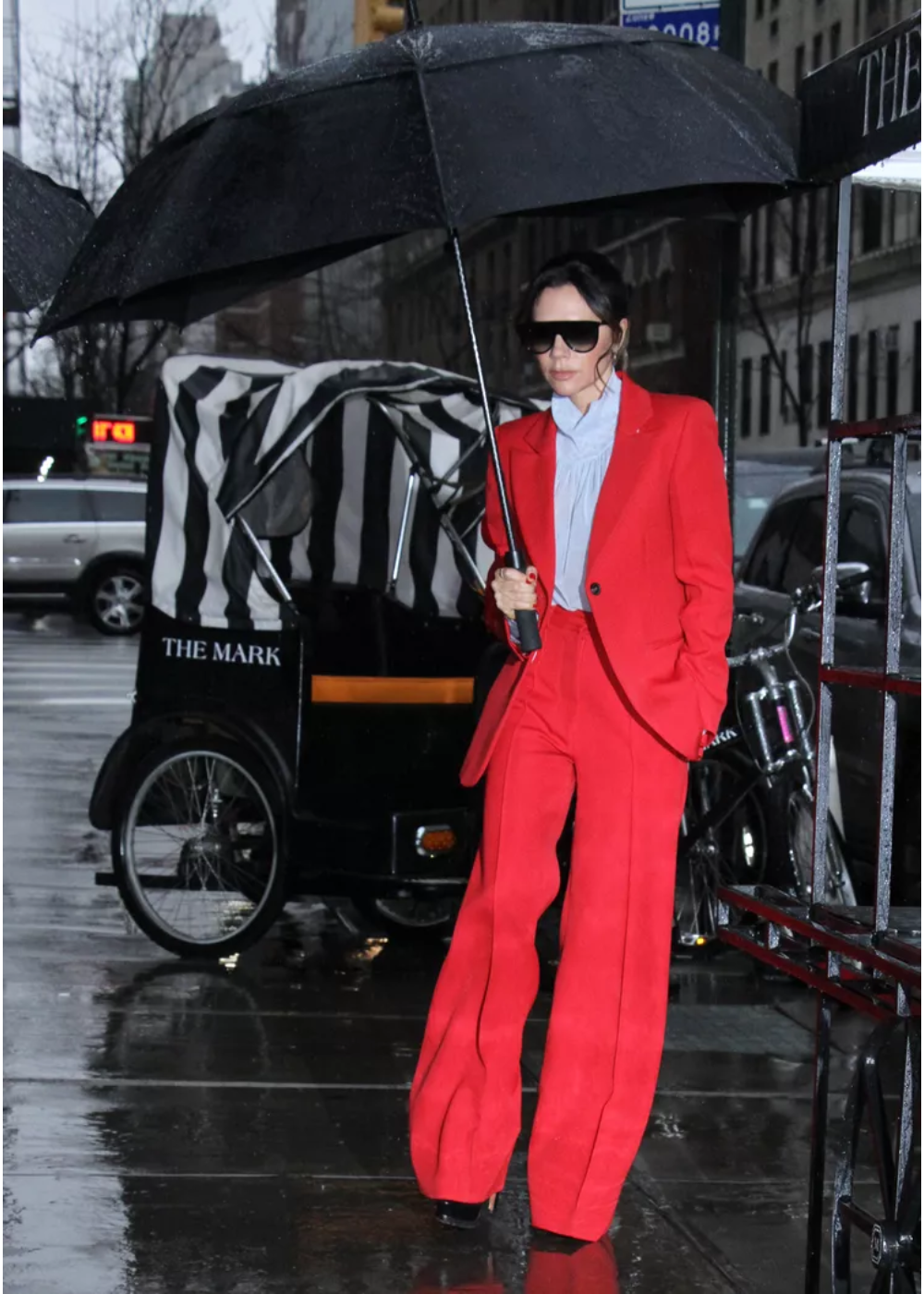 O look com terninho apresenta um conjunto vermelho vibrante, destacando-se em um dia chuvoso. A peça é composta por um blazer estruturado e calças largas, que conferem sofisticação e estilo. A blusa azul clara complementa o visual.
