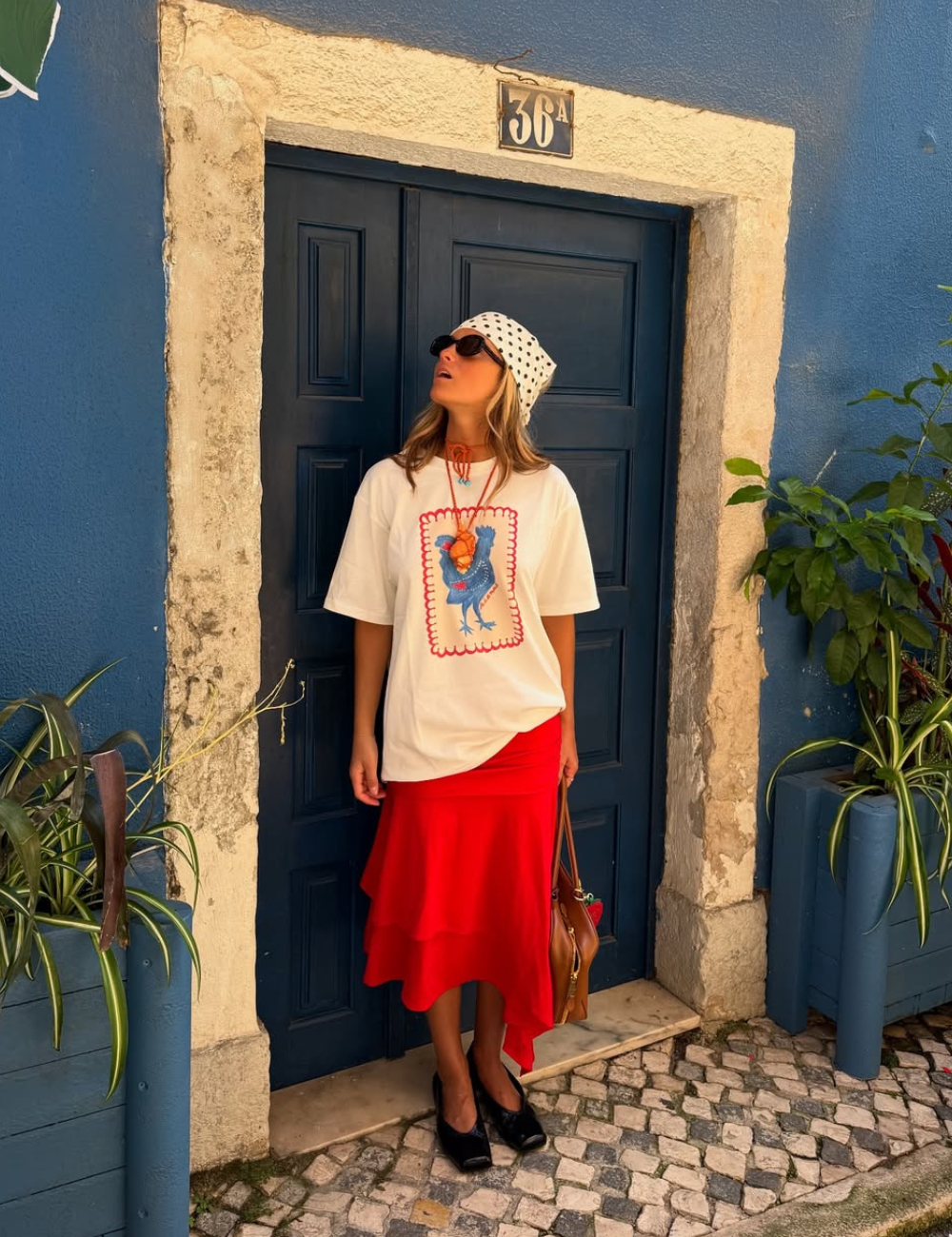 A combinação de uma t-shirt oversized com estampa colorida e uma saia vermelha fluida cria um look estiloso e descontraído. O uso de acessórios como óculos escuros e um lenço na cabeça adiciona charme e personalidade.