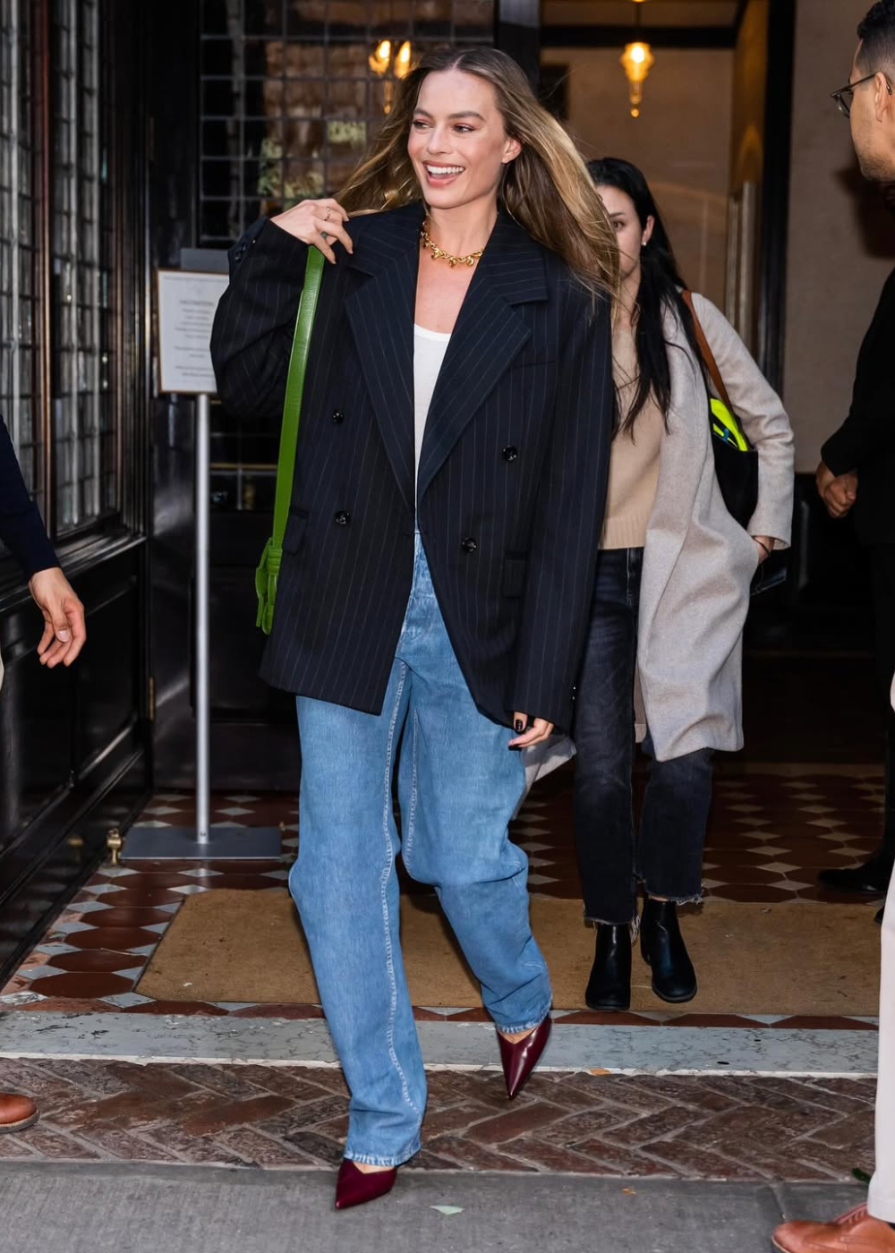 O look apresenta um blazer oversized listrado, combinado com uma camiseta básica branca e jeans de cintura alta, criando um visual casual e estiloso. O toque de elegância vem dos sapatos de salto vermelho, que adicionam um contraste vibrante.
