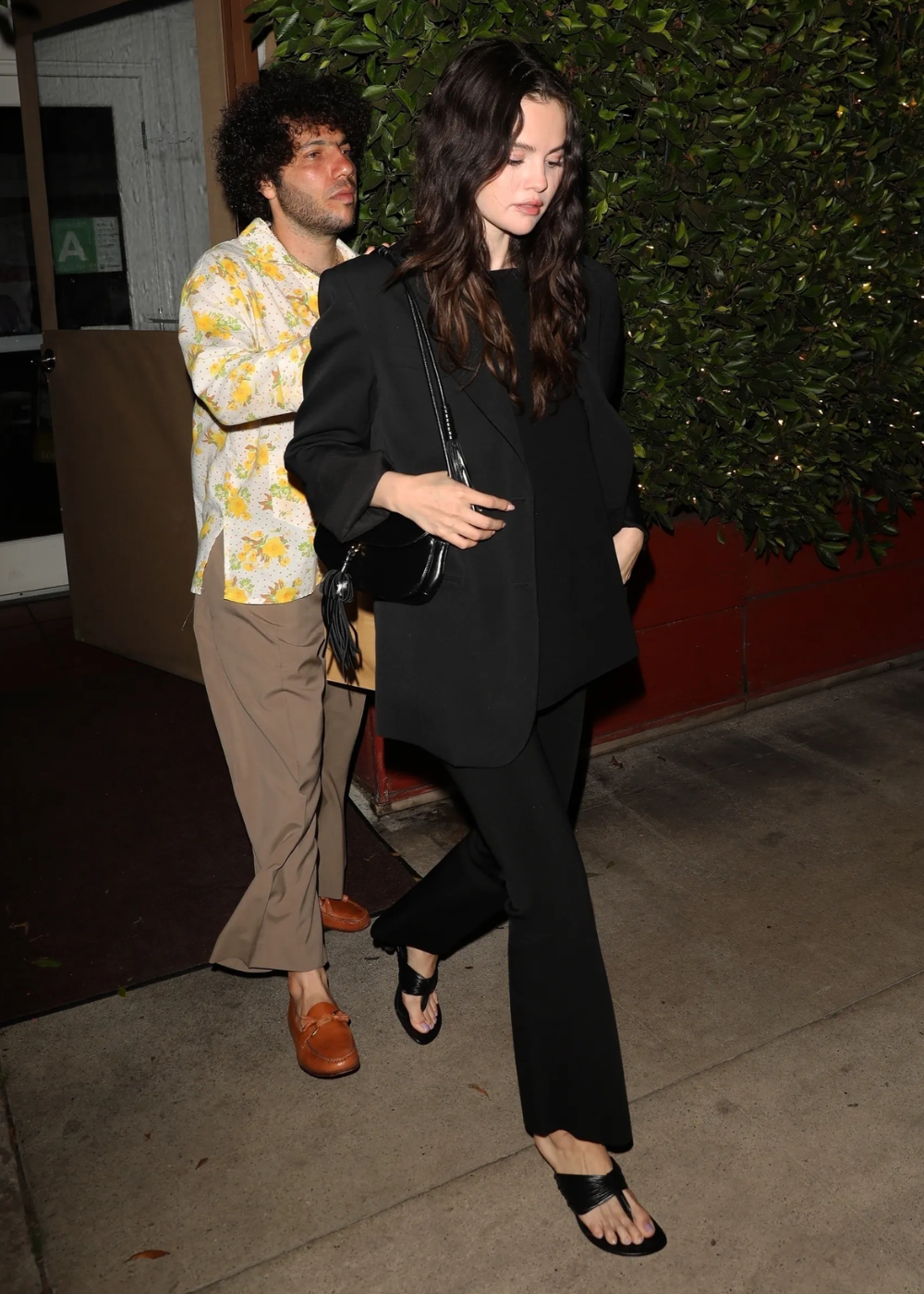 Um dos looks fáceis com blazer é exemplificado por uma mulher vestindo um blazer oversized preto, combinado com uma blusa e calça preta, criando uma silhueta elegante e minimalista. Ela usa sandálias de tiras pretas, complementando o visual.