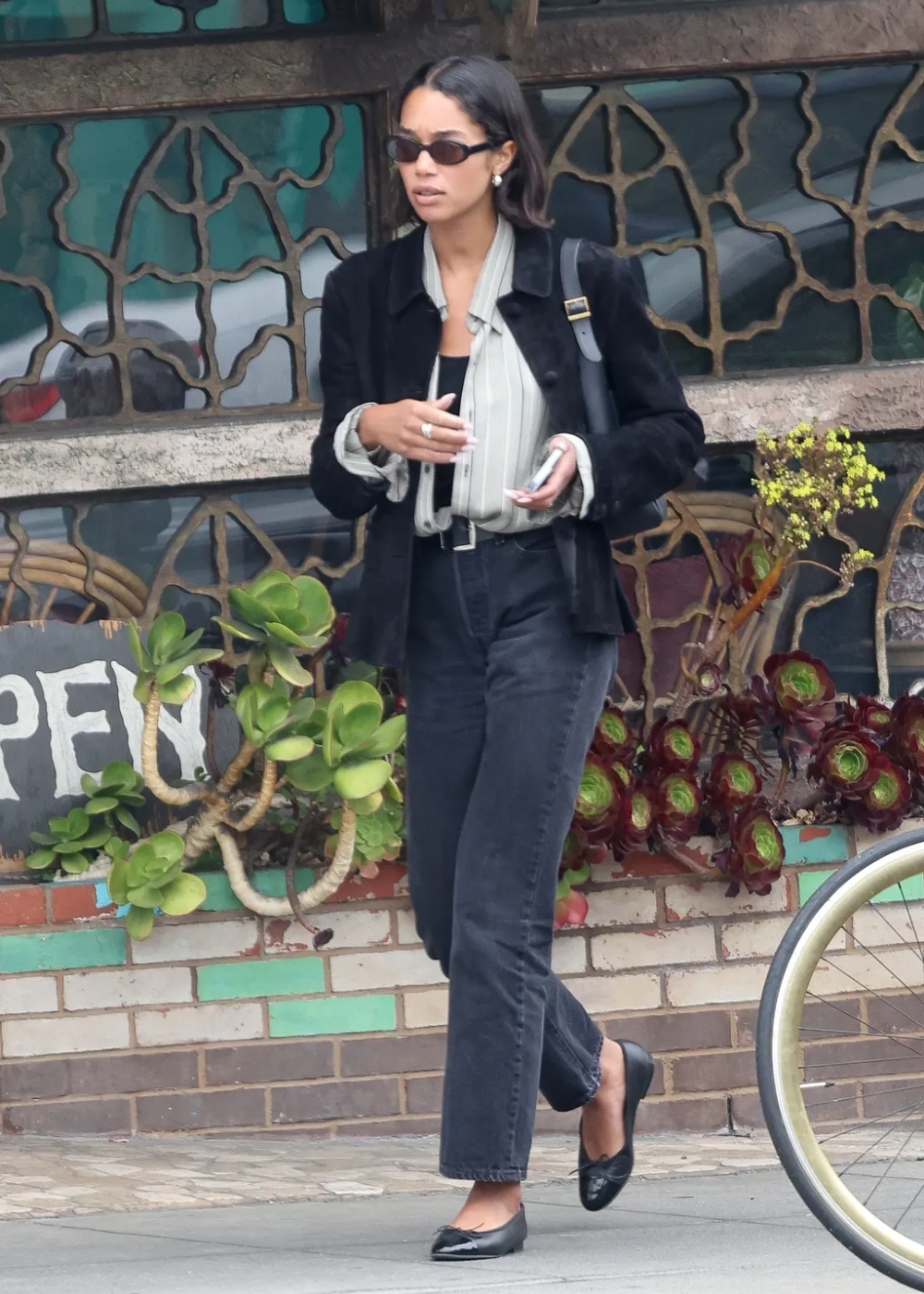 O look exibe um blazer preto sobre uma blusa de listras em tons claros, complementado por calças jeans escuras e sapatilhas pretas. A combinação traz sofisticação e conforto, ideal para diversas ocasiões.