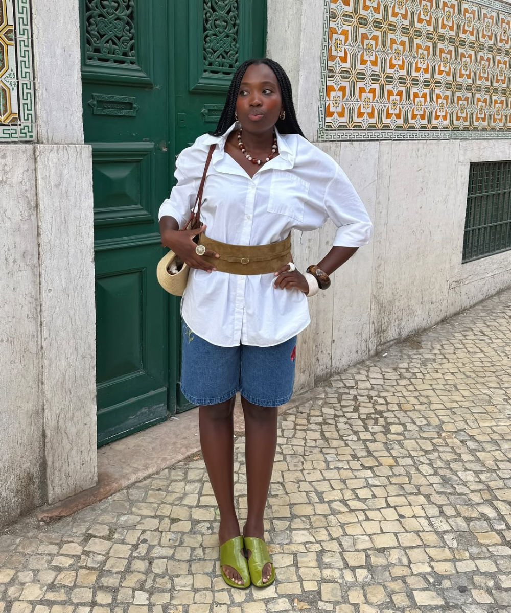 Pessoa com camisa branca, short jeans, sandálias verdes e cinto marrom, estilo casual.