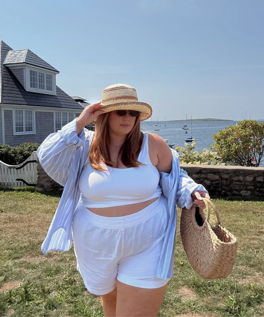 Pessoa com conjunto branco e chapéu de palha perto do mar. Looks fresquinhos com charme casual.