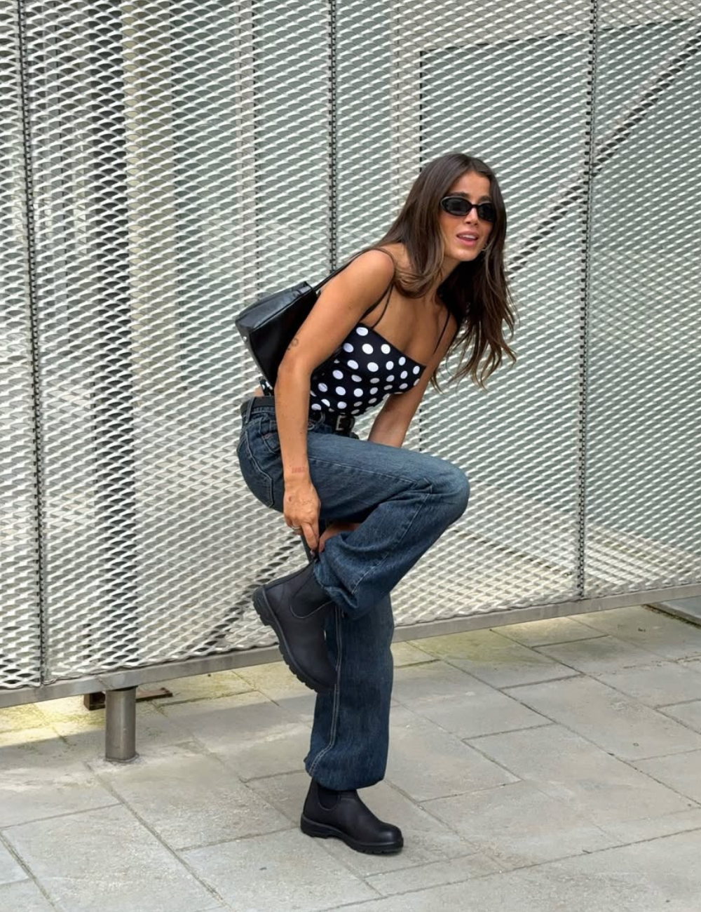 Looks para dias chuvosos com estilo: a combinação de um top de bolinhas em preto e branco, jeans largos e botas de borracha pretas traz conforto e elegância. Óculos escuros complementam o visual, ideal para enfrentar a umidade sem perder a sofisticação.