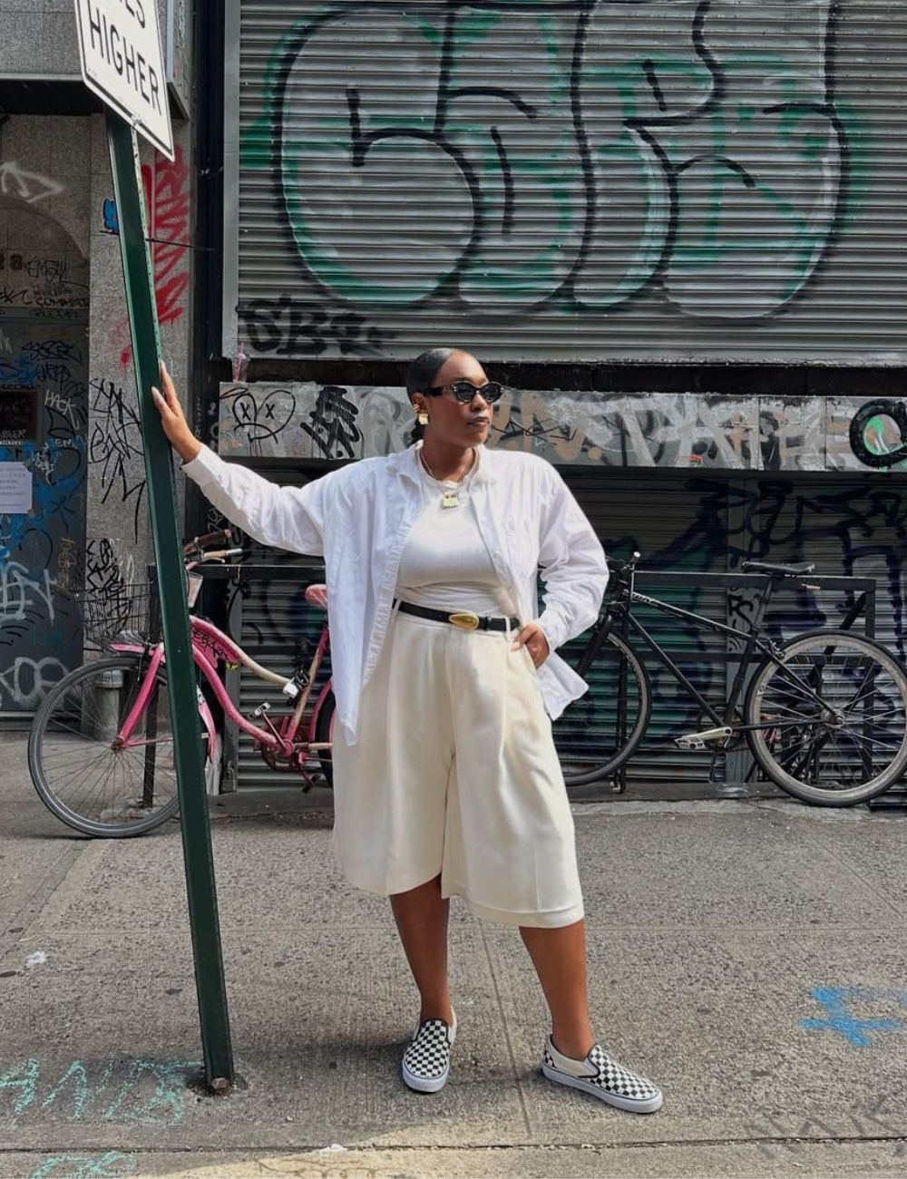 Look ideal para dias chuvosos, destacando conforto e estilo. A modelo veste uma camisa branca oversized, ideal para camadas, e um shorts largo em tom claro, proporcionando liberdade de movimento. Os tênis xadrez adicionam um toque moderno.