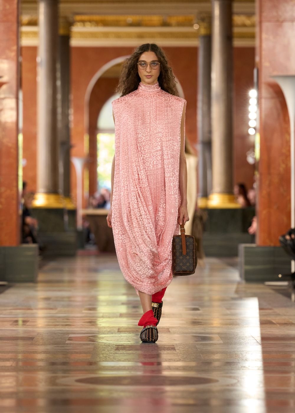 Vestido rosa bebê com textura usado em desfile, combinado com bolsa e sapatos estilosos.