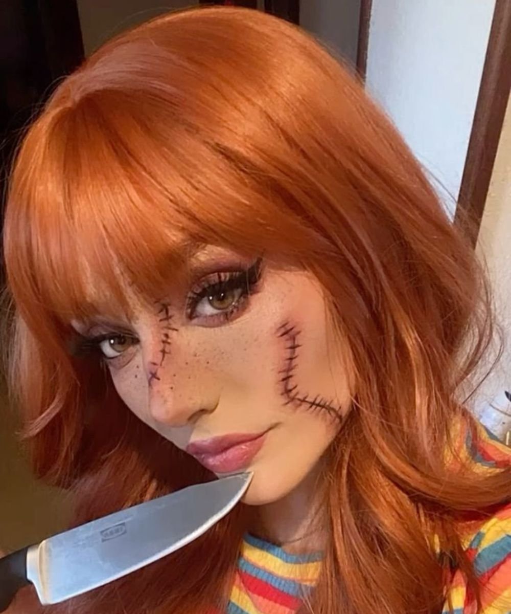 Mulher com maquiagem de Halloween inspirada em Chucky, apresentando uma pele pálida e marcas de costura realistas no rosto.