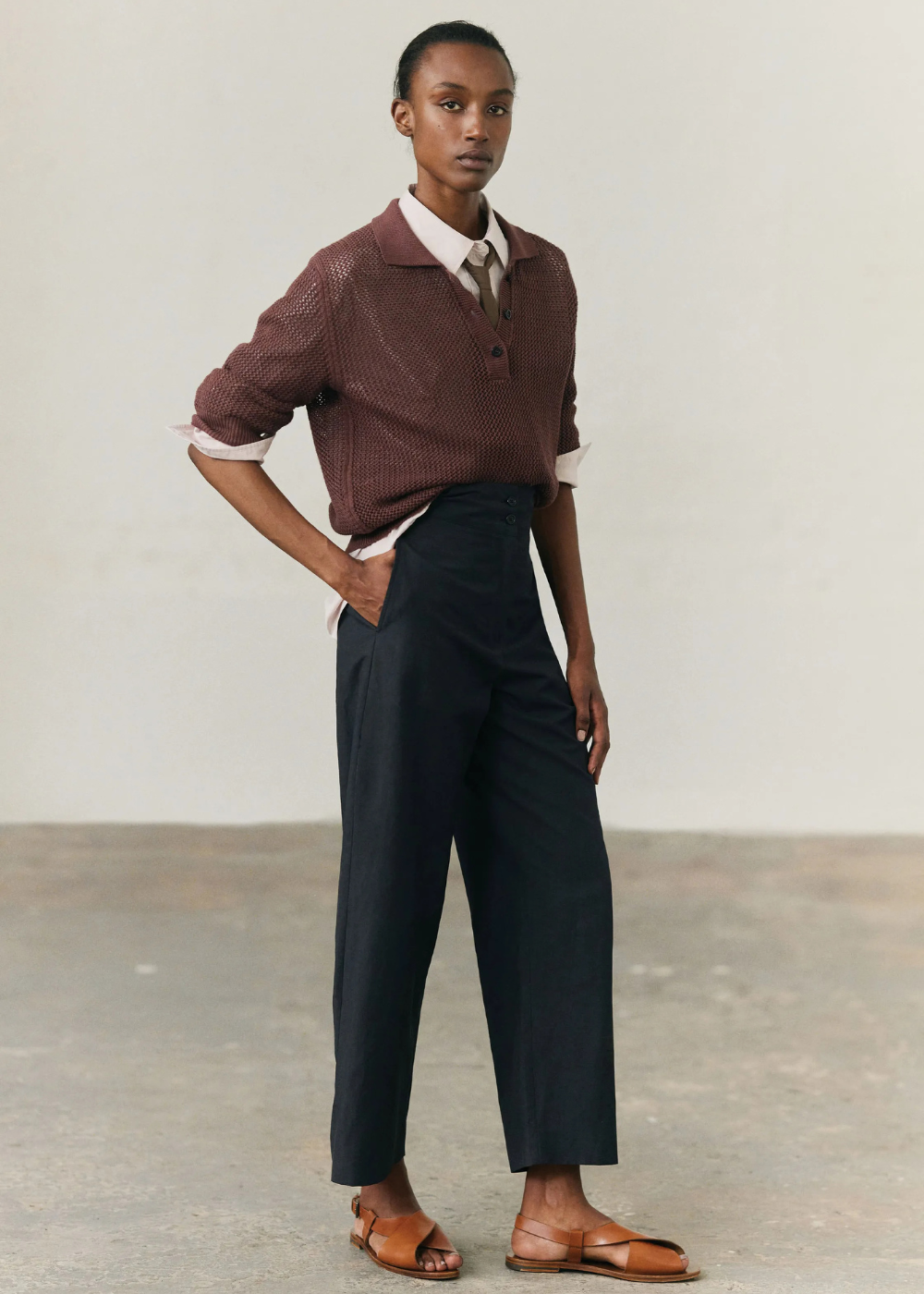 Pessoa vestindo camisa tipo blusa polo marrom com calça escura e sandálias marrom claro.
