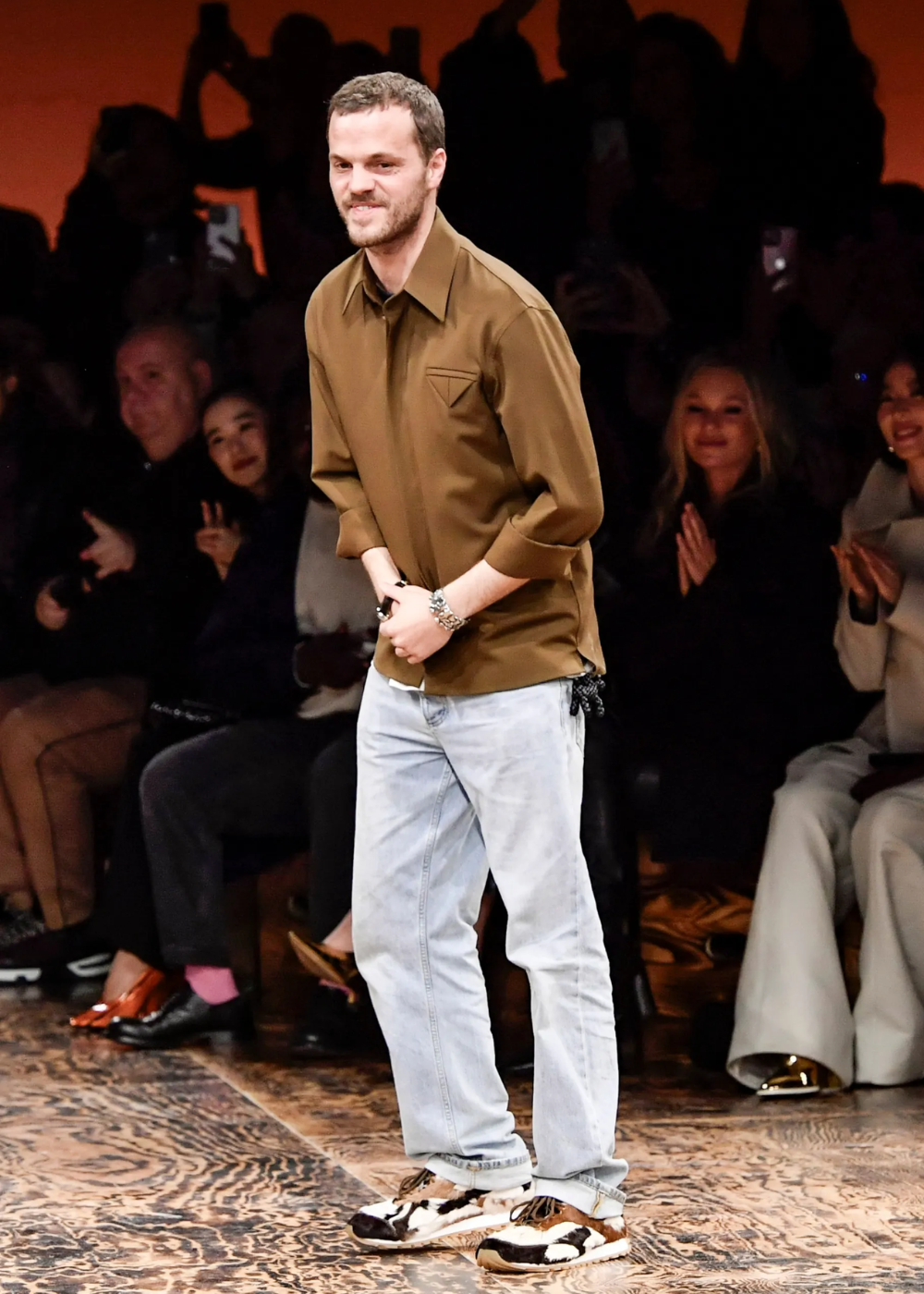 Matthieu Blazy de pé após desfile usando camisa marrom, jeans e tênis.