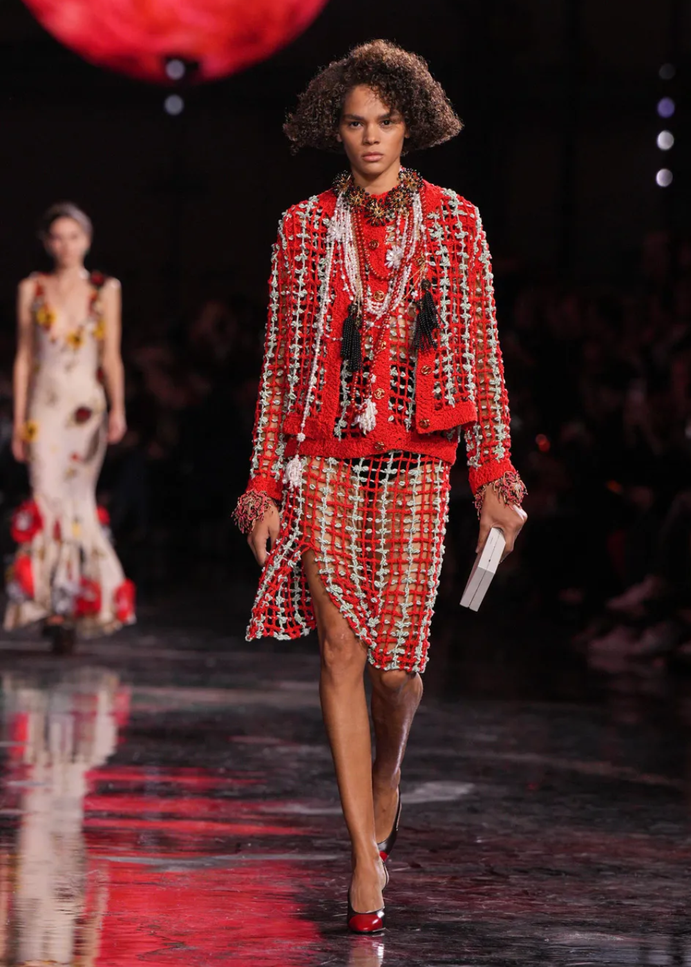 Modelo desfila em passarela usando conjunto vermelho com detalhes trançados e colares com motivo de Matthieu Blazy.