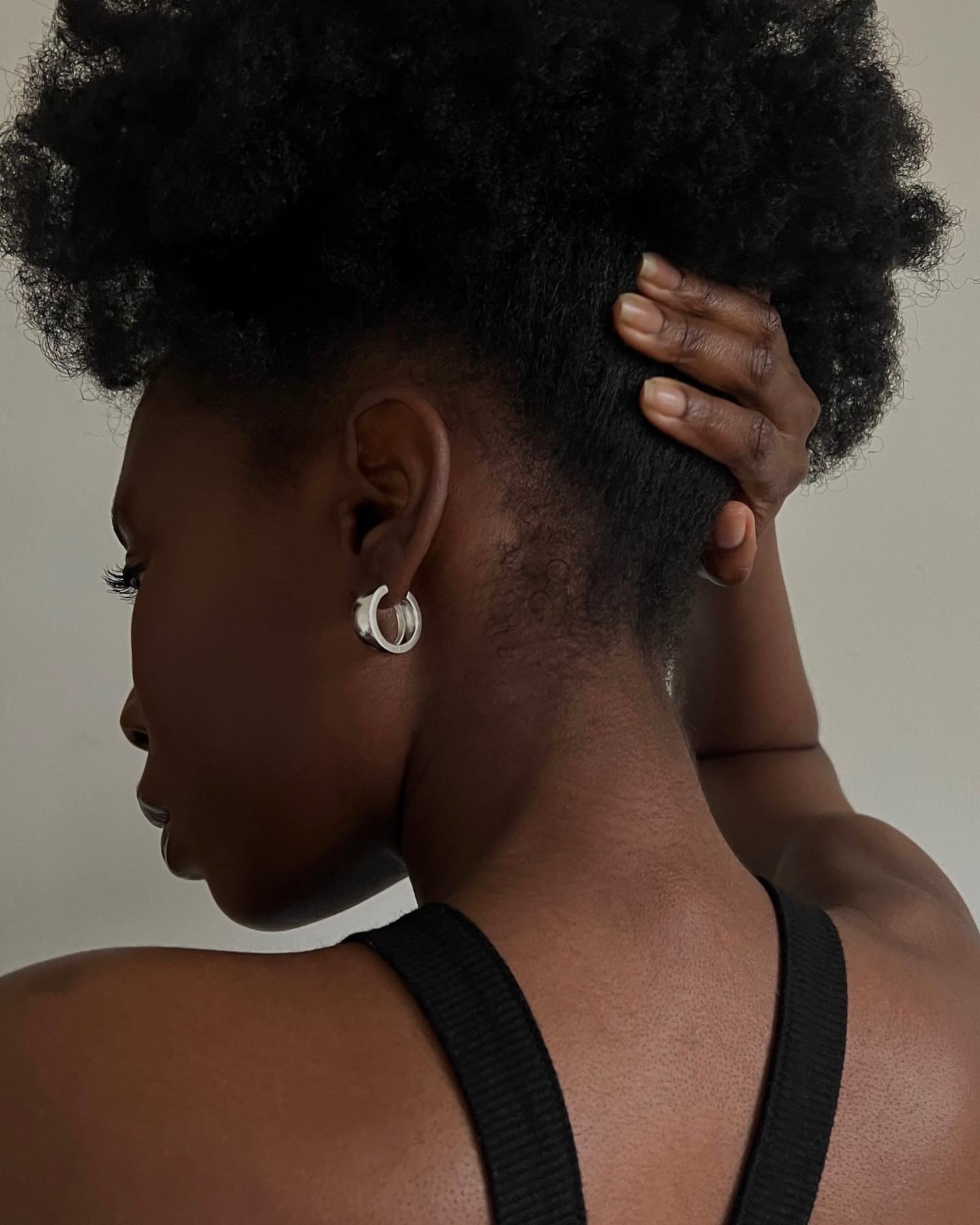 Mulher de perfil, segurando cabelo, com brinco prateado e blusa preta. Representa uma foto de perfumes franceses.
