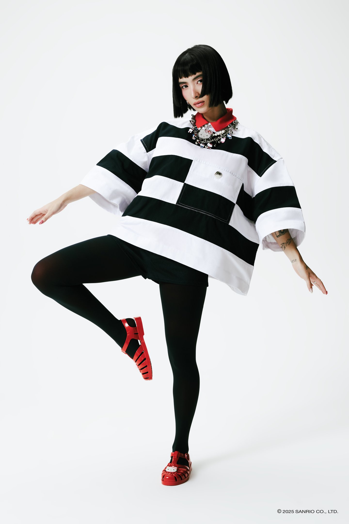 Modelo com cabelo curto usa camiseta listrada, sandália Melissa vermelha com detalhe da Hello Kitty.collab Melissa e Hello Kitty