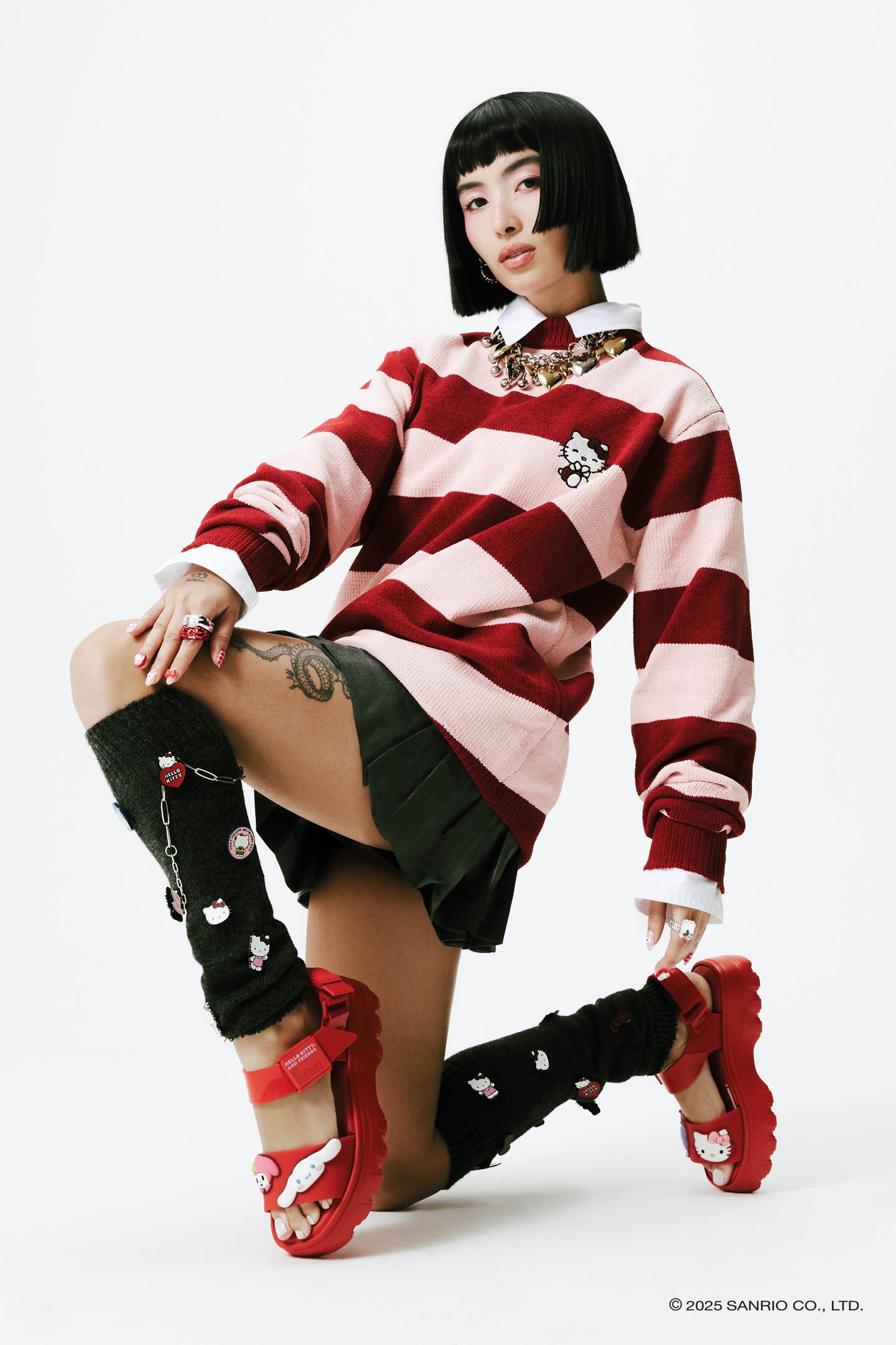 Pessoa usando blusa listrada com Hello Kitty, sandálias Melissa vermelhas e meias decoradas com temas Hello Kitty. collab Melissa e Hello Kitty