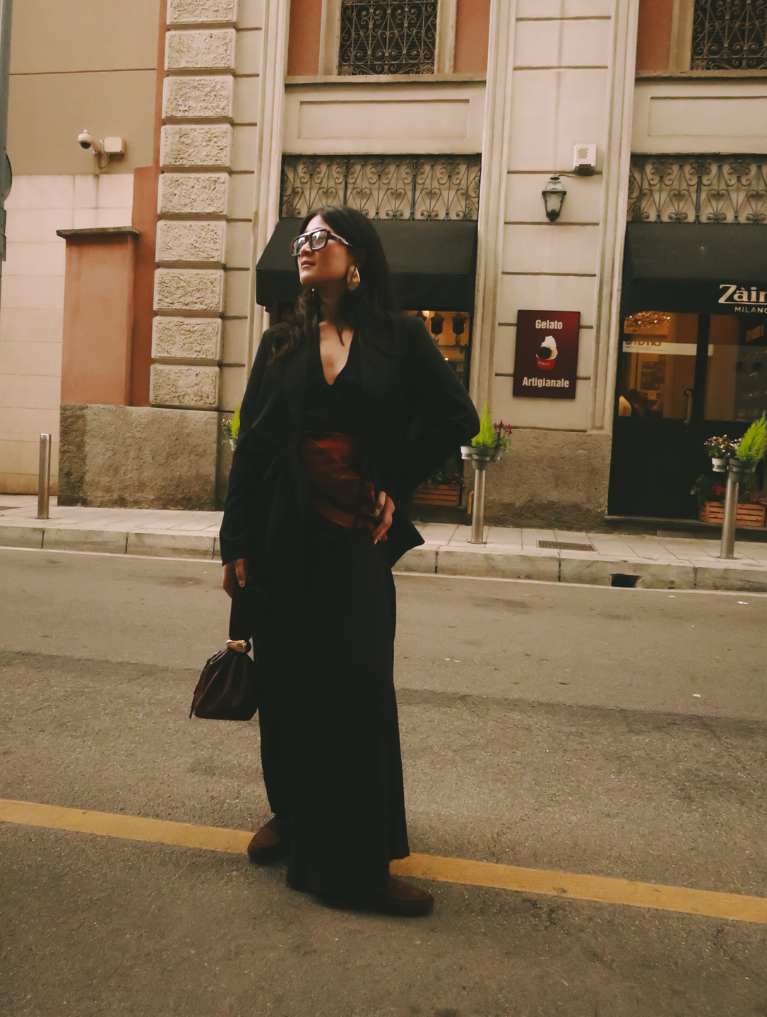 Pessoa de óculos escuros com roupa elegante em frente a um restaurante na Milão Fashion Week.