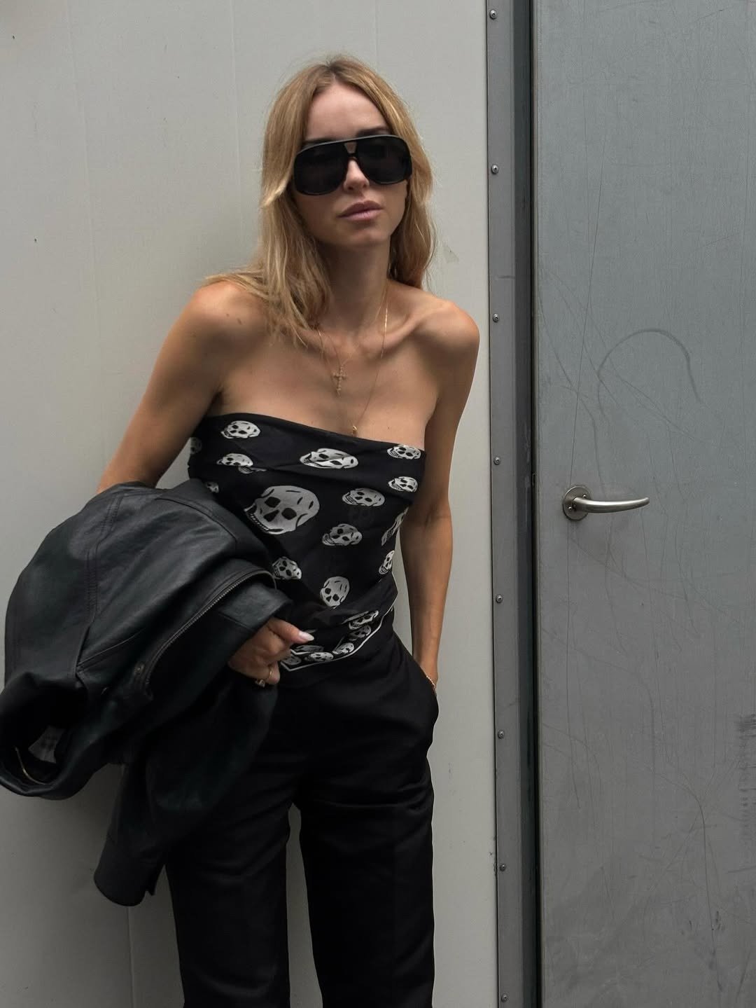 Na moda anos 2010, destaca-se um look ousado com blusa sem alças estampada com caveiras, refletindo a estética punk e rock. A combinação com calças pretas de alfaiataria e jaqueta de couro cria um visual moderno e elegante.