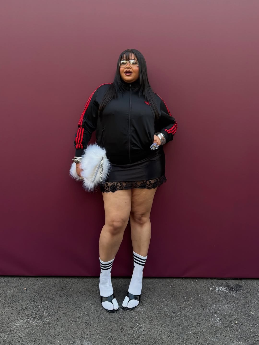 A moda anos 2010 é marcada por combinações ousadas e influências streetwear. A imagem apresenta uma mulher vestindo um conjunto esportivo da Adidas, com detalhes em vermelho, complementado por uma mini saia preta com renda.