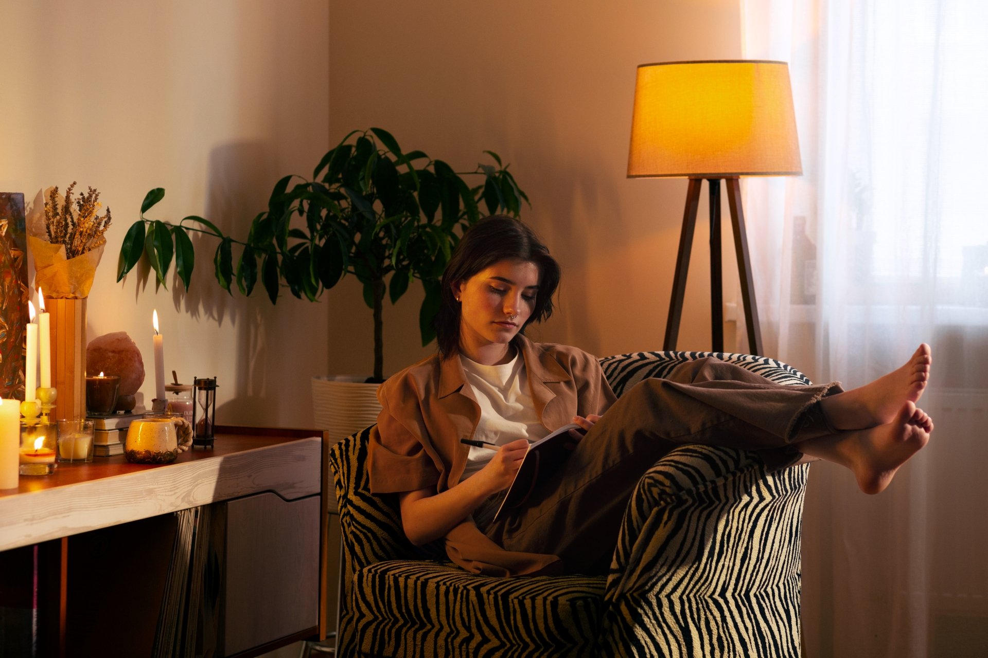 Mulher relaxa em poltrona com estampa zebrada, sob lâmpada quente, ao lado de plantas. Moda e design de interiores