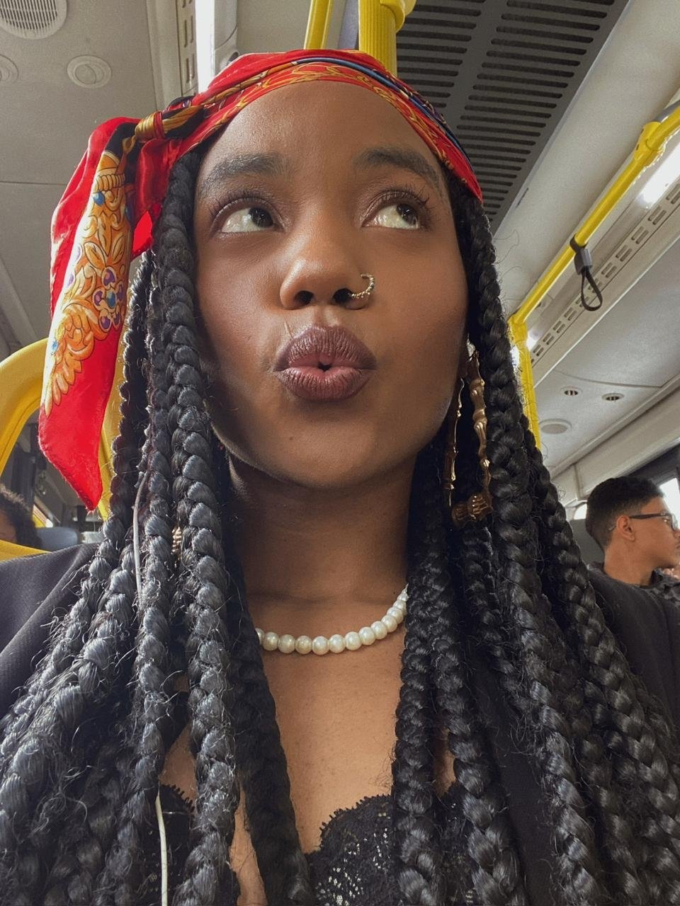 Usuária com tranças e lenço colorido está em um transporte público, olhando pela janela.