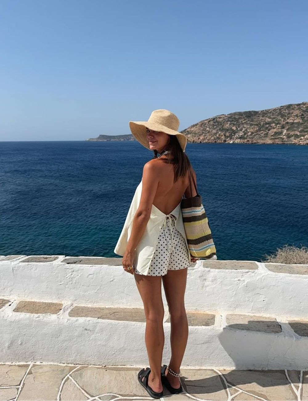 Uma das tendências moda praia 2026 destaca-se pela combinação de estilo e conforto. A modelo, com um vestido leve e de alças, exibe um design que valoriza a silhueta, enquanto o chapéu de palha oferece proteção solar.