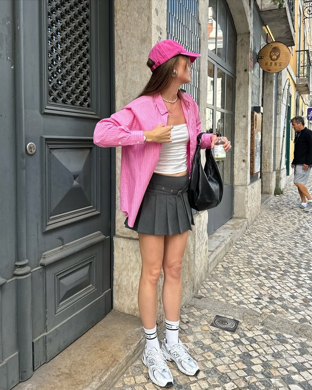 A imagem destaca uma jovem em um look estiloso para o verão, usando uma blusa rosa listrada aberta sobre uma camiseta branca. Modelos de blusa para verão