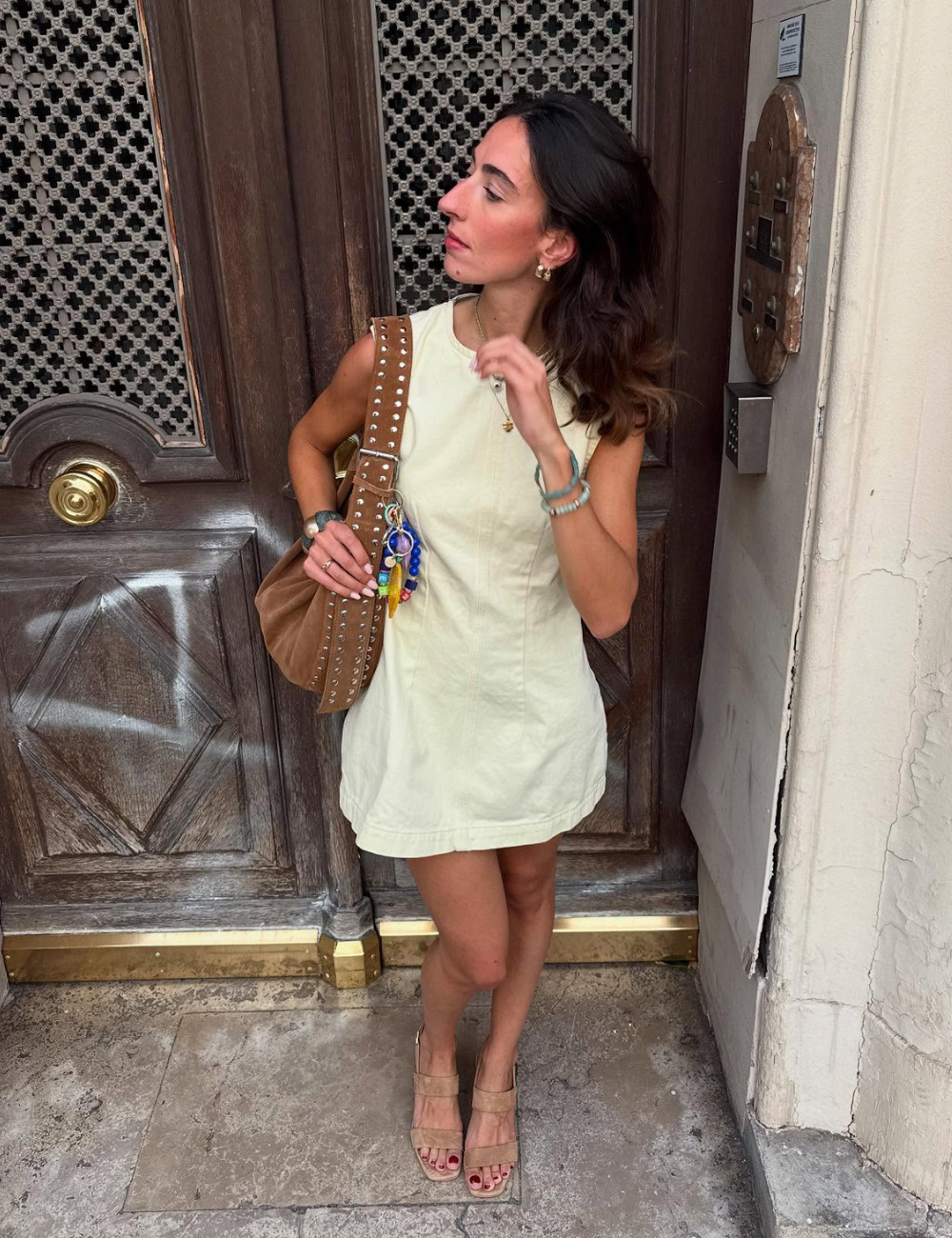 Vestido bege e bolsa marrom com tachas, uma combinação de modelos de bolsa tendência na moda.