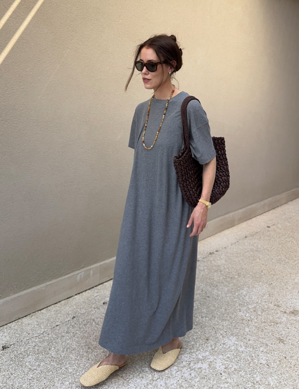 Mulher com vestido cinza e bolsa de crochê marrom, modelos de bolsa tendência, usando óculos escuros.