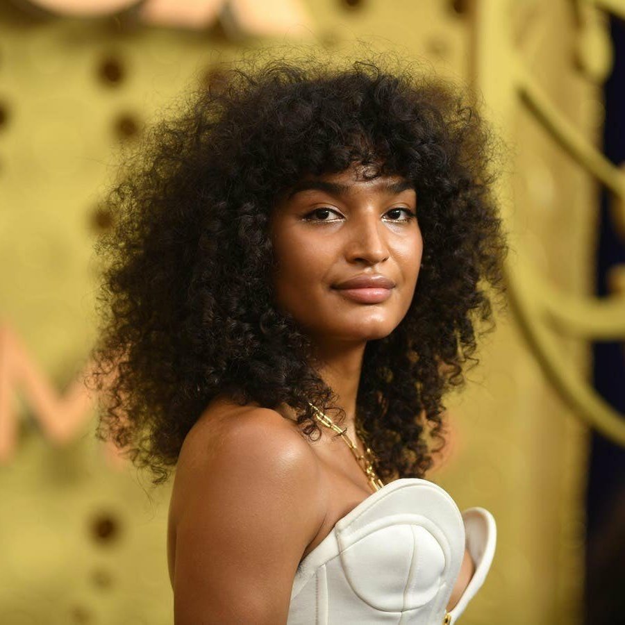 Cabelo cacheado volumoso com franja em destaque, estilo moderno e elegante.