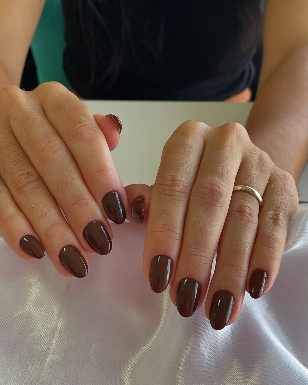 As unhas apresentam um esmalte descasque em tom marrom profundo, com acabamento brilhante.