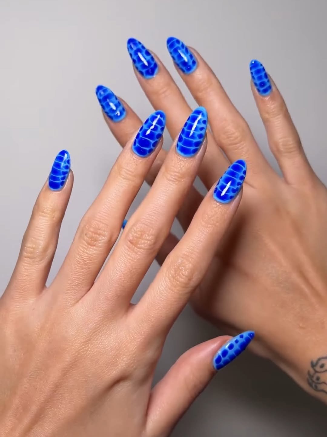 As unhas exibem um esmalte descasque vibrante, em tom azul, com um design que imita escamas.