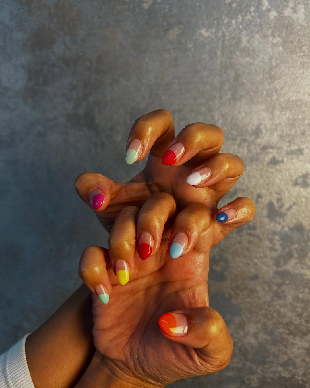 As unhas exibem uma combinação vibrante de esmaltes, com cores como vermelho, azul, amarelo e verde, criando um efeito divertido e moderno.