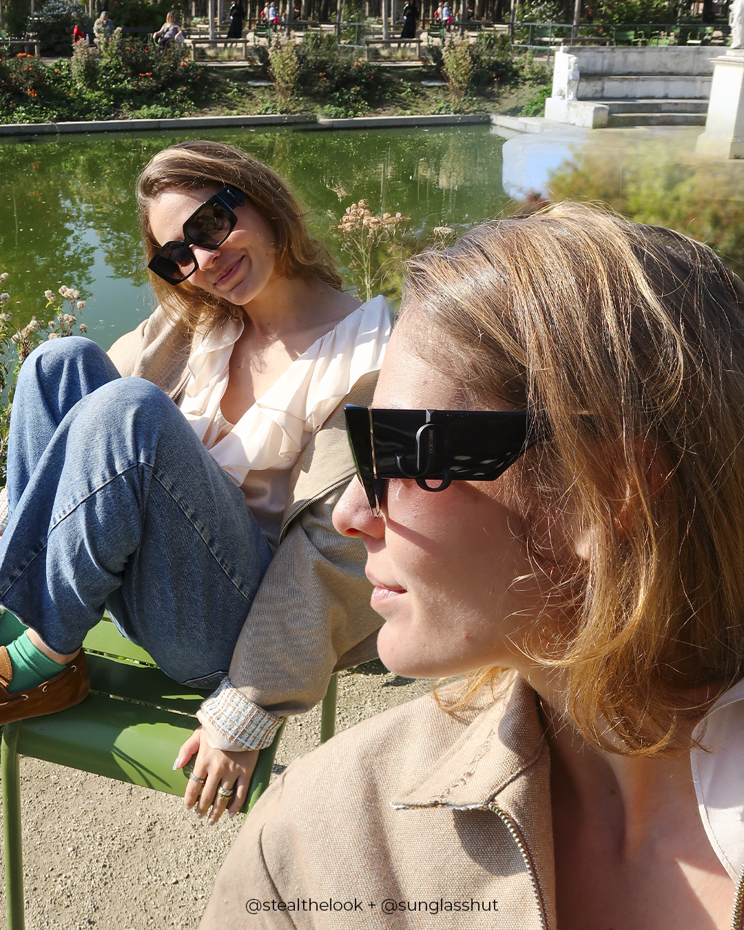 Amigas em um parque, usando óculos de sol tendência, sentadas em cadeiras verdes ao lado de um lago.