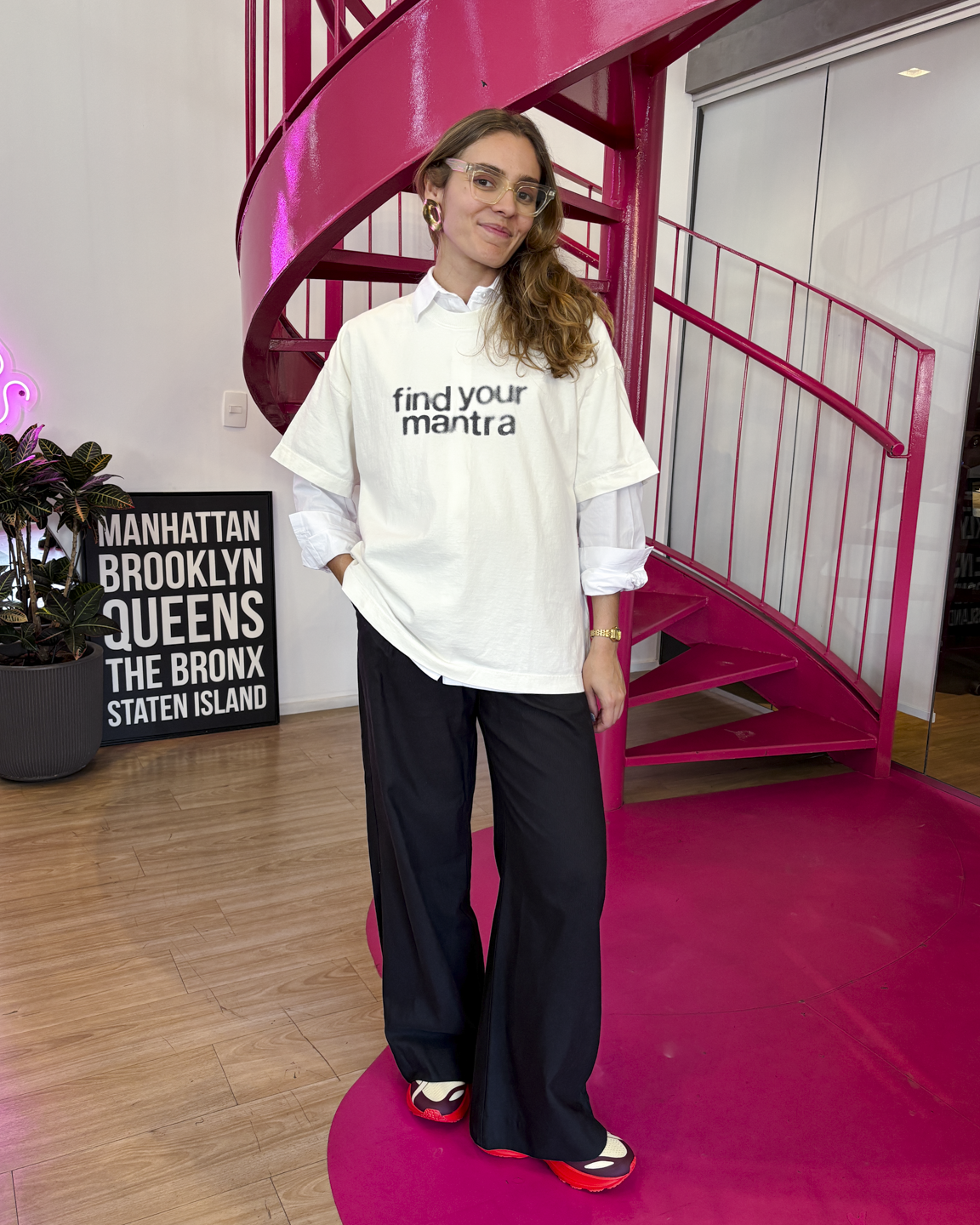 Pessoa com looks esportivos e estilosos, usando camiseta branca. Ela está em frente a uma escada rosa.