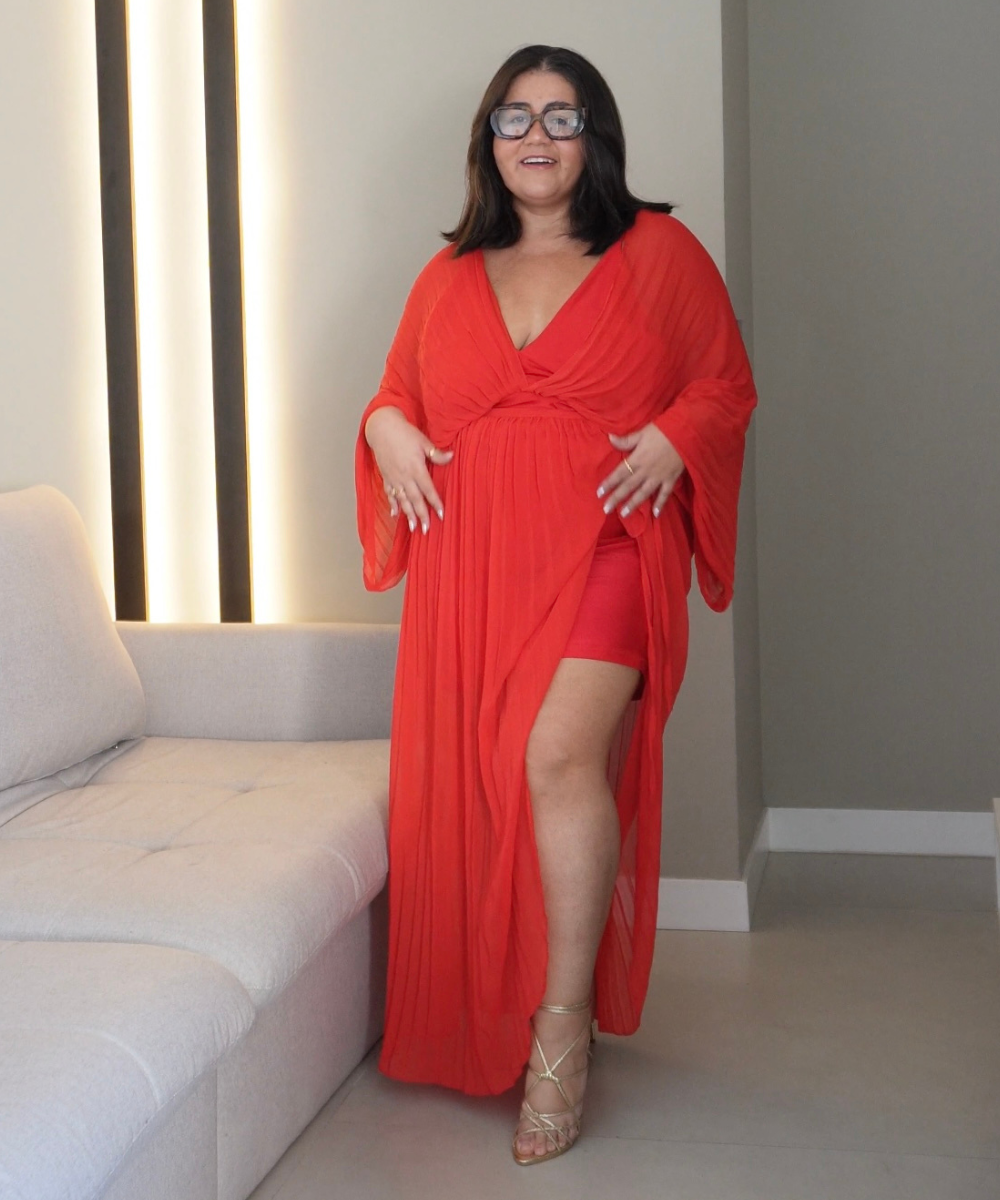 Usuária vestindo um look vermelho elegante ao lado de um sofá claro. Perfume invisível captura a essência vibrante.