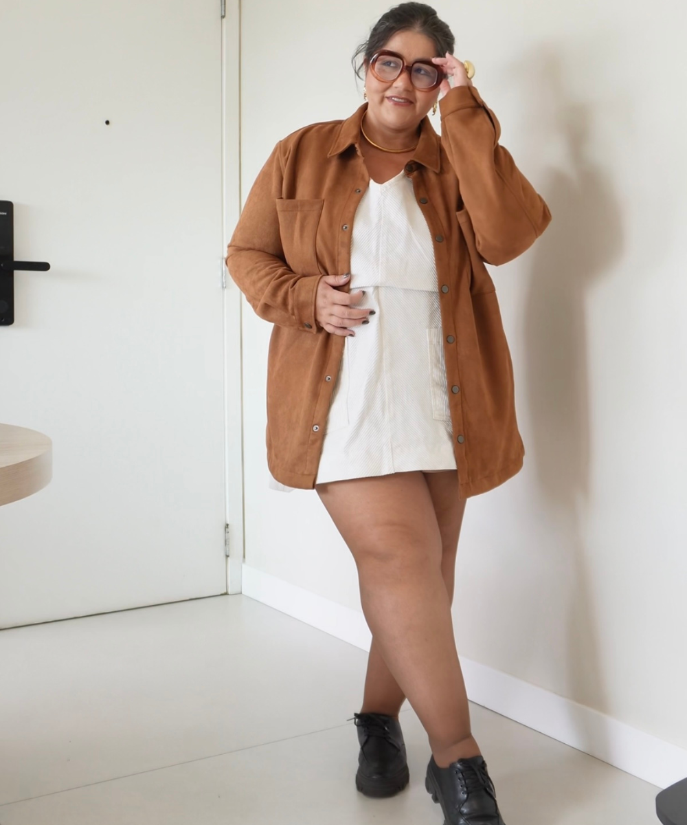 Pessoa com óculos de grau e look casual: camisa marrom sobre vestido branco e sapatos pretos. Juntando perfume e look.