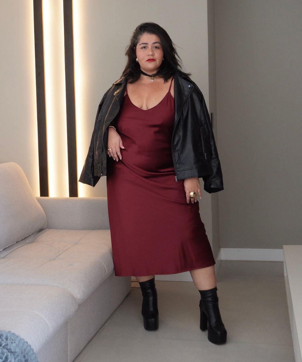 Mulher com look elegante, vestido vinho e jaqueta preta. O ambiente sugere um aroma envolvente de perfume.