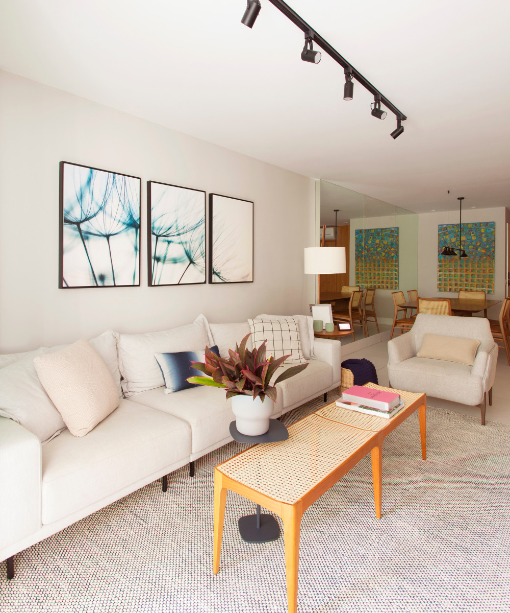 Sala com sofá claro, almofadas coloridas e mesa de centro com plantas. Quadros azuis como destaque na decoração.