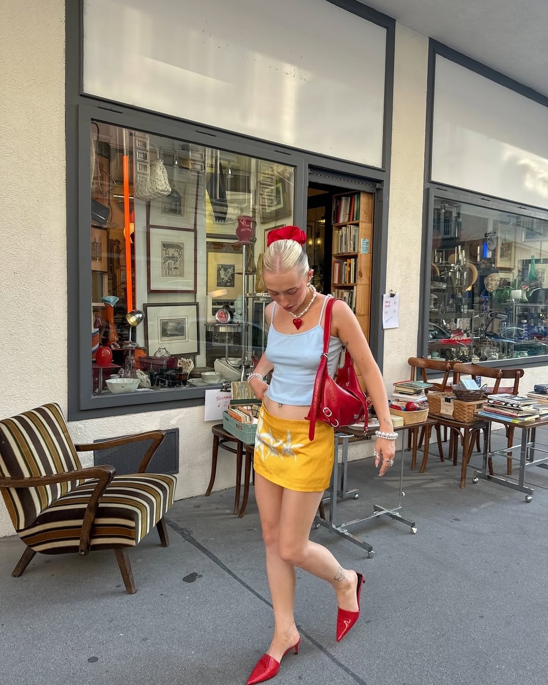 A regata curtinha em tom azul claro combina perfeitamente com a saia amarela, destacando um look jovem e moderno. A modelo usa sapatos vermelhos e uma bolsa da mesma cor, criando um contraste vibrante.