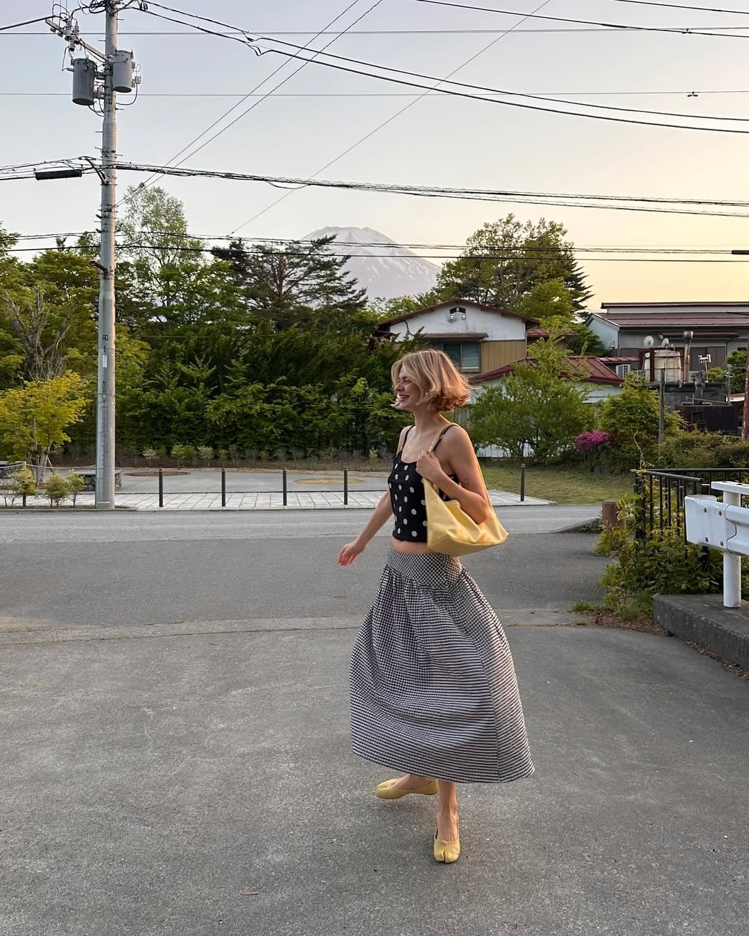 A regata curtinha em estilo cropped, com estampa de bolinhas, combina perfeitamente com a saia longa listrada, criando um look leve e moderno. O uso de acessórios, como a bolsa amarela, adiciona um toque de cor, ideal para dias ensolarados.