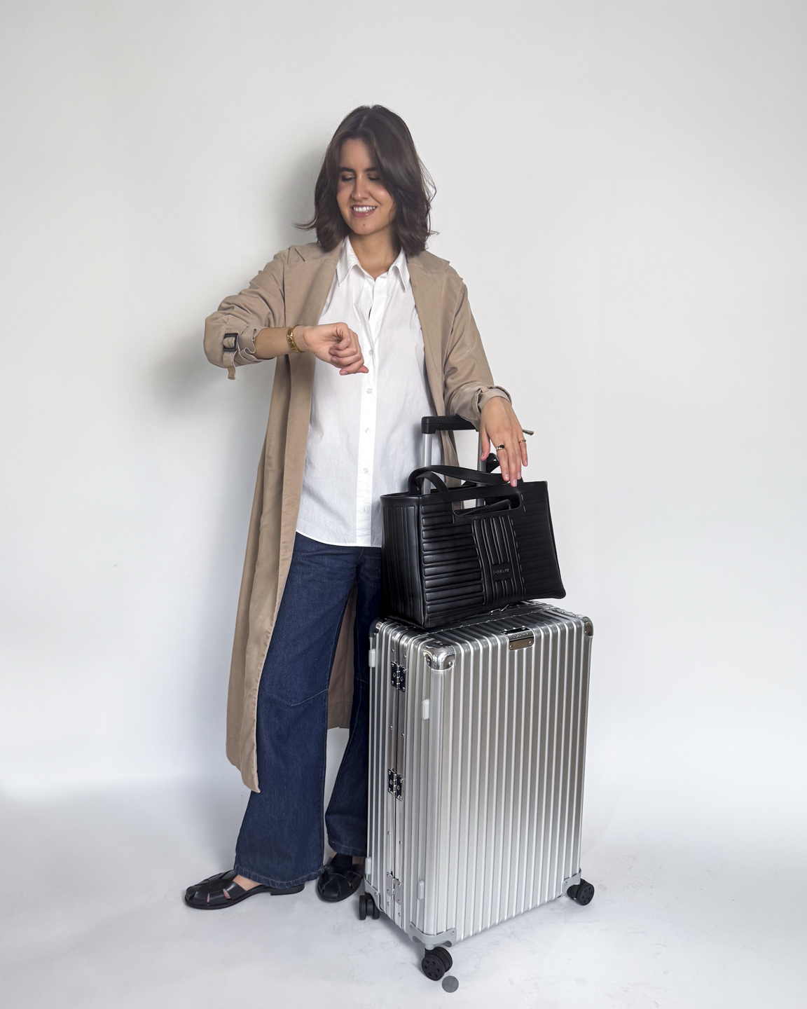 mulher usando calça jeans, camisa branca e trench coat bege, em look de aeroporto estiloso