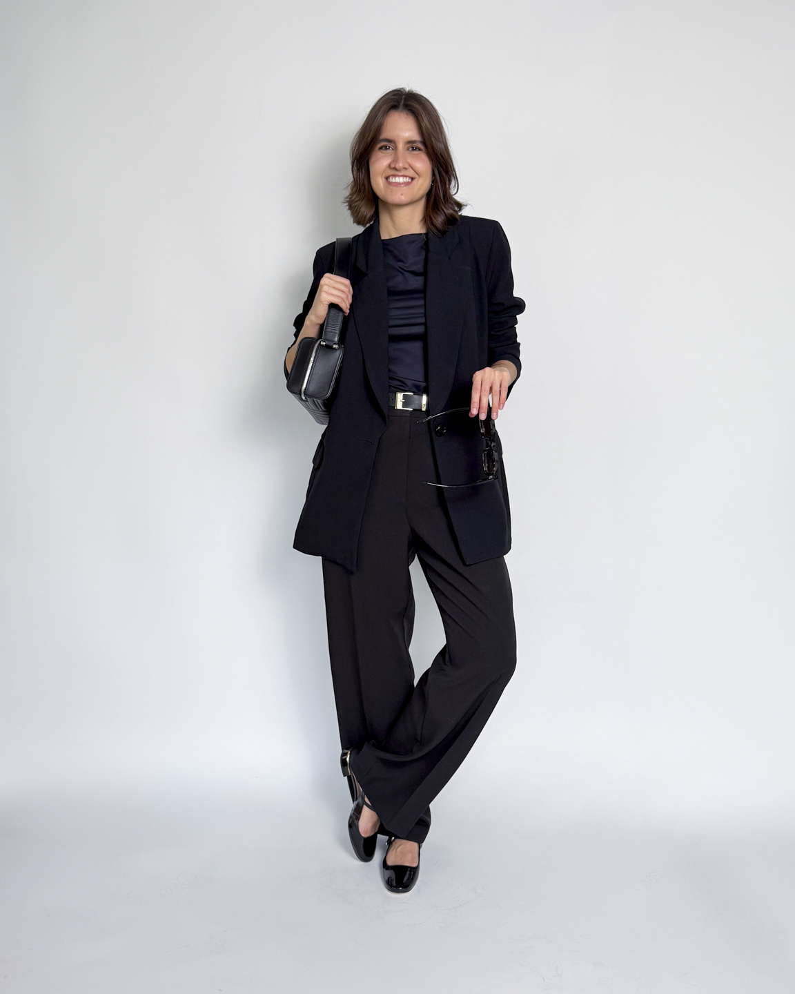 mulher usando calça de alfaiataria, regata preta e blazer preto, em look de aeroporto estiloso