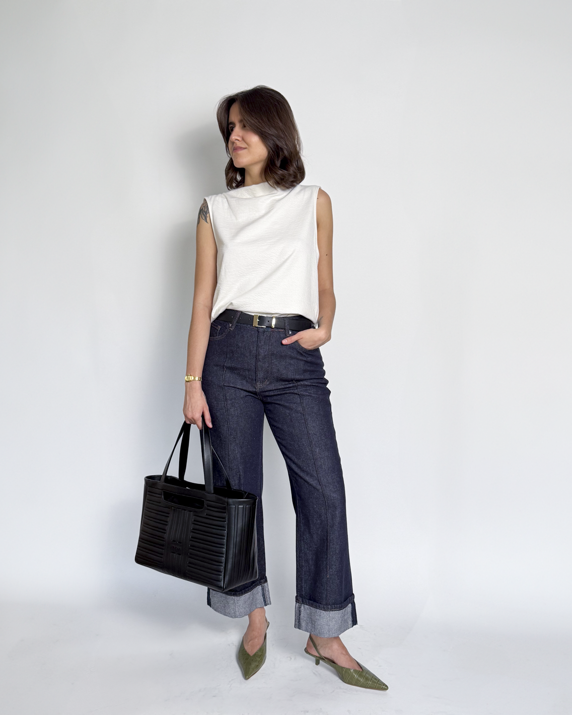 mulher com calça jeans, regata branca e bolsa preta em um look de aeroporto estiloso