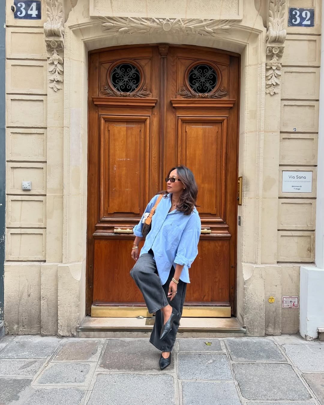 A imagem apresenta uma mulher estilosa usando uma sapatilha bico fino preta, que complementa seu look moderno. Ela veste uma camisa azul clara e calças largas, criando um contraste elegante.