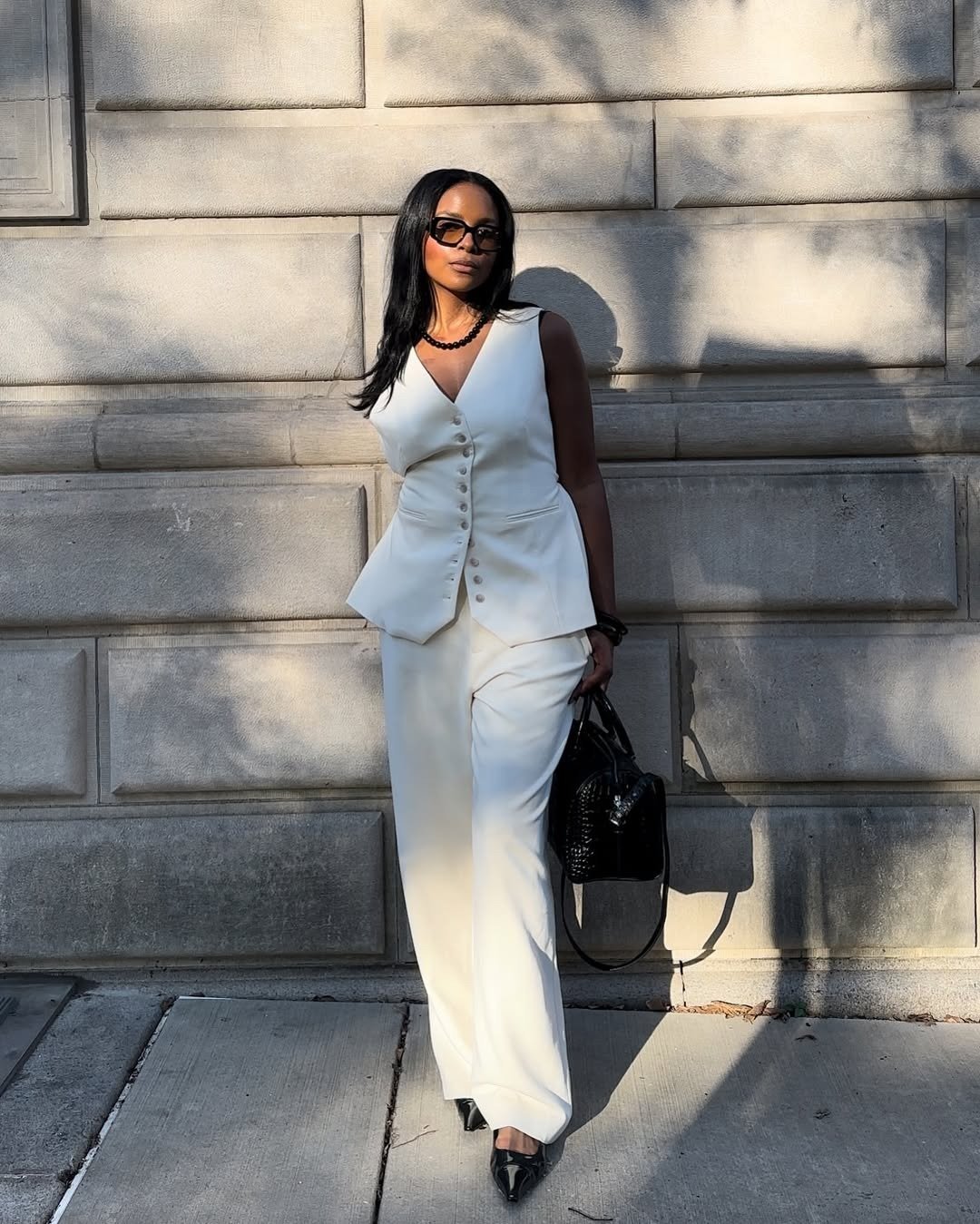 A imagem apresenta uma mulher elegante vestindo um conjunto branco, composto por um colete com botões e calças amplas. Nos pés, destaca-se uma sapatilha bico fino, que complementa o visual sofisticado.