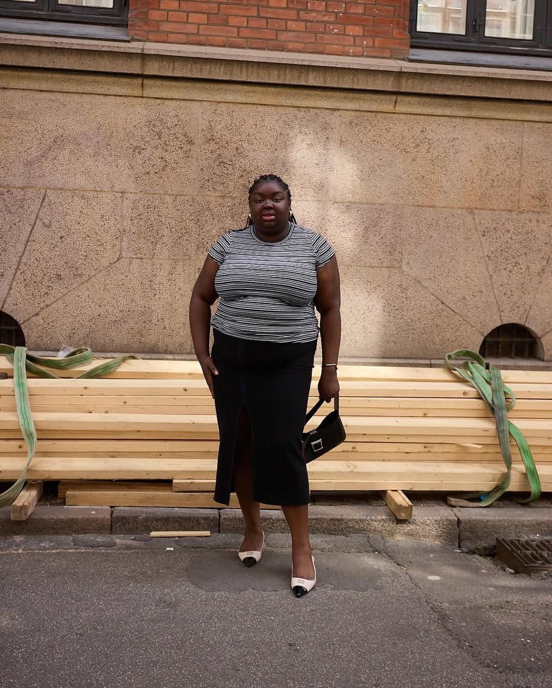 A imagem apresenta uma mulher em um cenário urbano, usando uma sapatilha bico fino que combina elegância e conforto. A peça é em tom claro, com detalhe em preto na ponta, ideal para compor looks sofisticados.