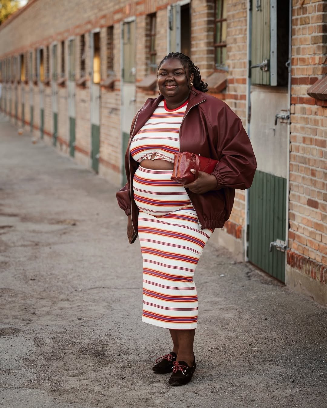 A imagem apresenta uma mulher confiante, usando um conjunto listrado em tons de vermelho e branco, que destaca sua silhueta com sapatos tendência 2026
